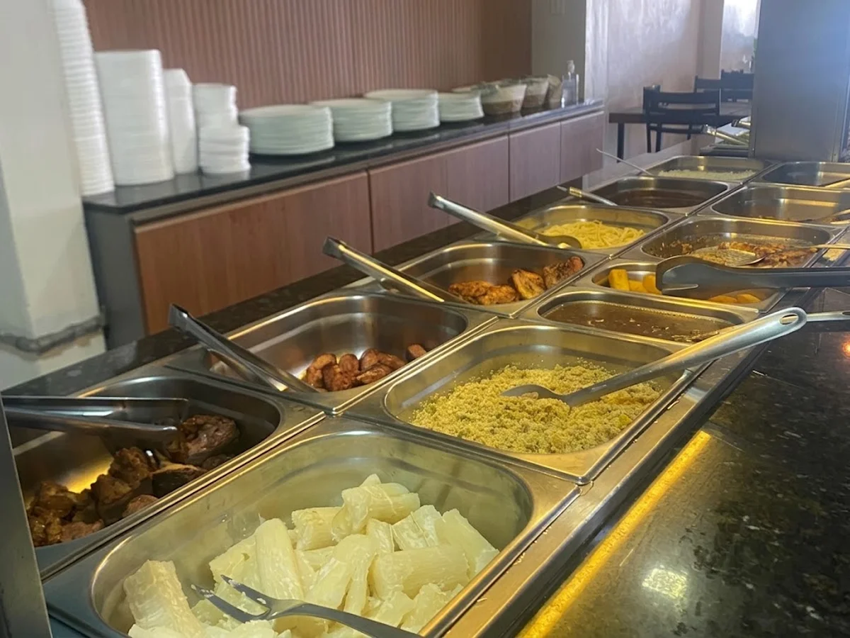 Balcão do buffet por quilo com pratos empilhados e acompanhamentos